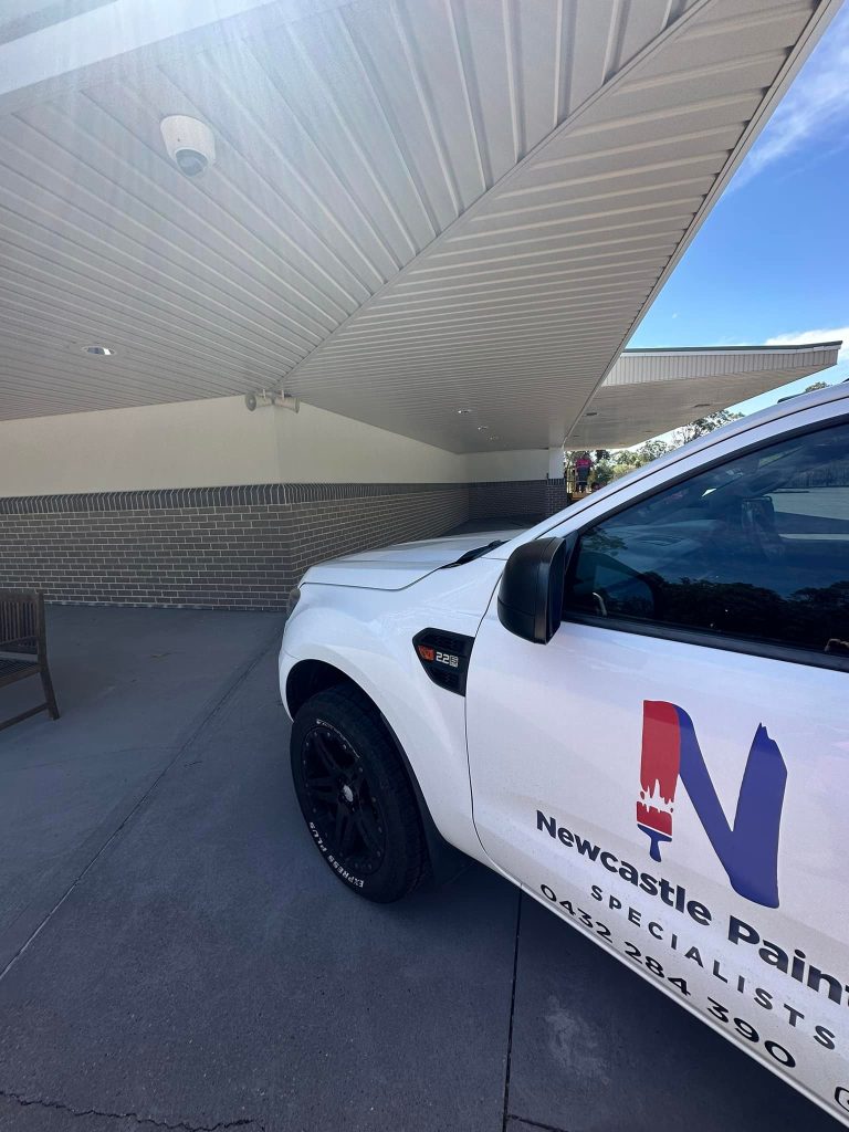 Photo of Newcastle Painting Specialists business Ute with their logo on the car and in the background a commercial painting project completed in Newcastle